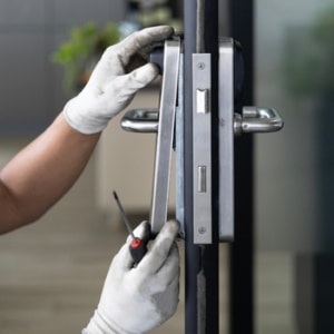 A person wearing white gloves is fixing a door handle as part of a lock replacement.