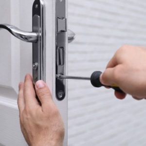 A locksmith is using a screwdriver to fix a door handle by unscrewing the locks on the door.