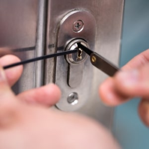 A locksmith uses a key to open a metal door while repairing a broken lock with special tools.