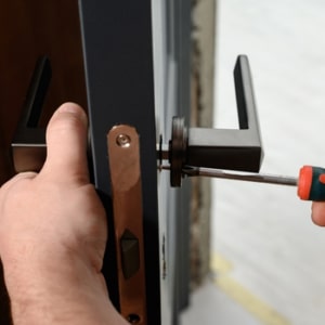 A locksmith uses a screwdriver to remove a door handle for changing the locks on a door.